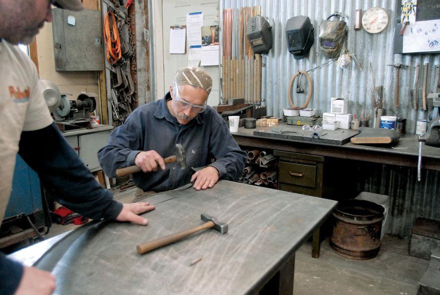 FILE- In this April 8, 2010, file photo, Darrin Beaudett, left, holds a piece of carbon steel steady as blacksmith Jeffrey Funk hammers the metal into a groove where a steel wire will be contained in the construction of a hand fabricated fender for a refurbished 1925 Glacier National Park tour bus in Kalispell, Mont. Eighty years later the buses still climb Going-to-the-Sun Road every summer, giving visitors from around the world tours of scenic Glacier National Park. (Lido Vizzutti/Flathead Beacon via AP, File) MANDATORY CREDIT