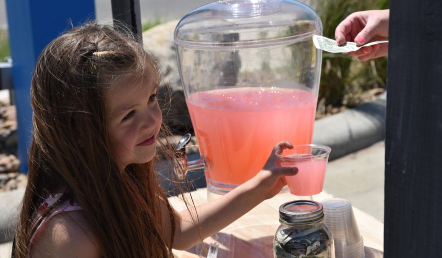 In this June 18, 2016, photo, Kira LeBaron hands out lemonade to a customer during the second annual Williston Lemonade Day in Williston, N.D. Area children set up street-side lemonade stands to learn about the fundamentals of operating a business. (Melissa Krause/Williston Herald via AP) MANDATORY CREDIT