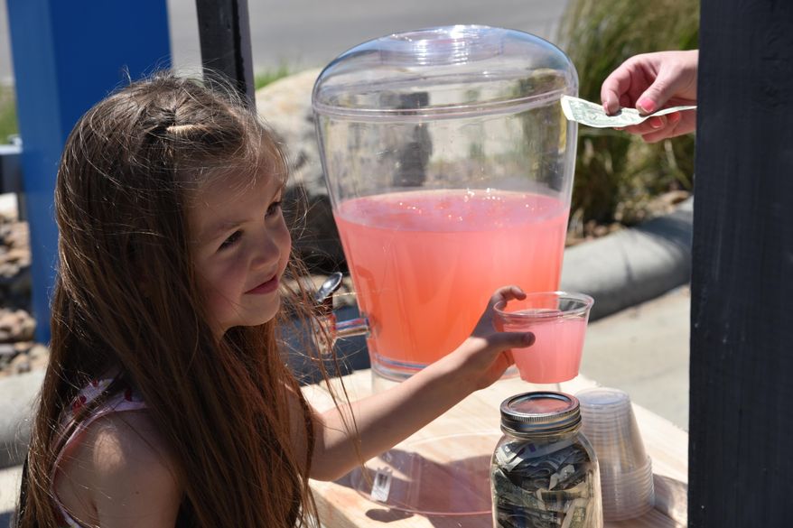 In this June 18, 2016, photo, Kira LeBaron hands out lemonade to a customer during the second annual Williston Lemonade Day in Williston, N.D. Area children set up street-side lemonade stands to learn about the fundamentals of operating a business. (Melissa Krause/Williston Herald via AP) MANDATORY CREDIT