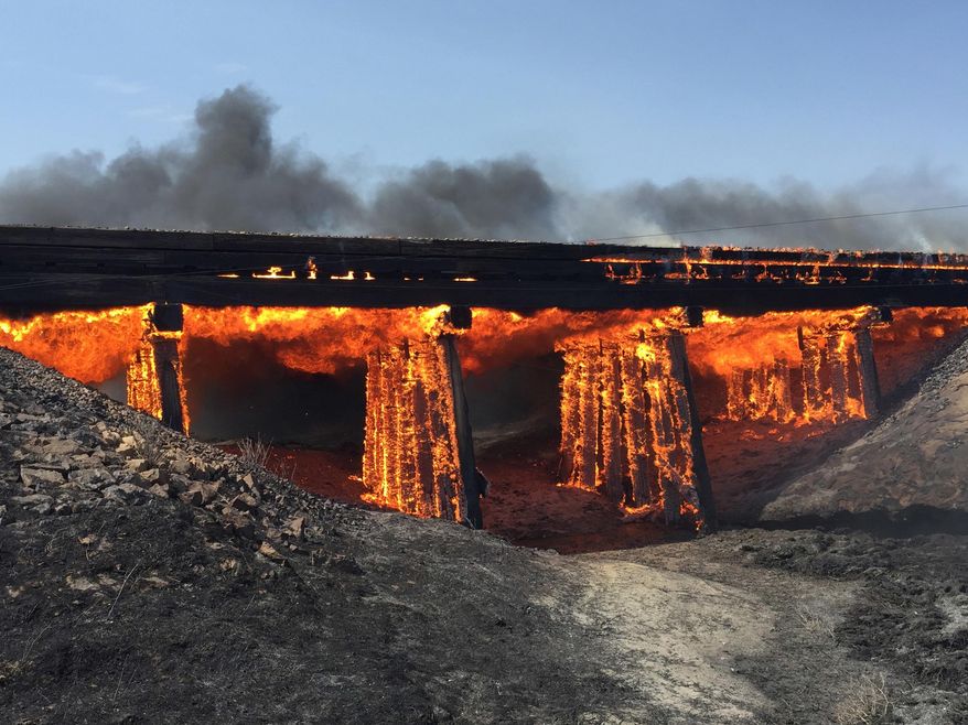 In this photo provided by Kiowa County, Colo., Sheriff Casey Sheridan, a railroad trestle burns near the tiny town of Haswell, Colo., Wednesday, June 22, 2016. For days, wildfires have raged amid spiking heat across Southern California and much of the West, forcing many to evacuate. (Casey Sheridan/Kiowa County, Colo., Sheriffs Department via AP)