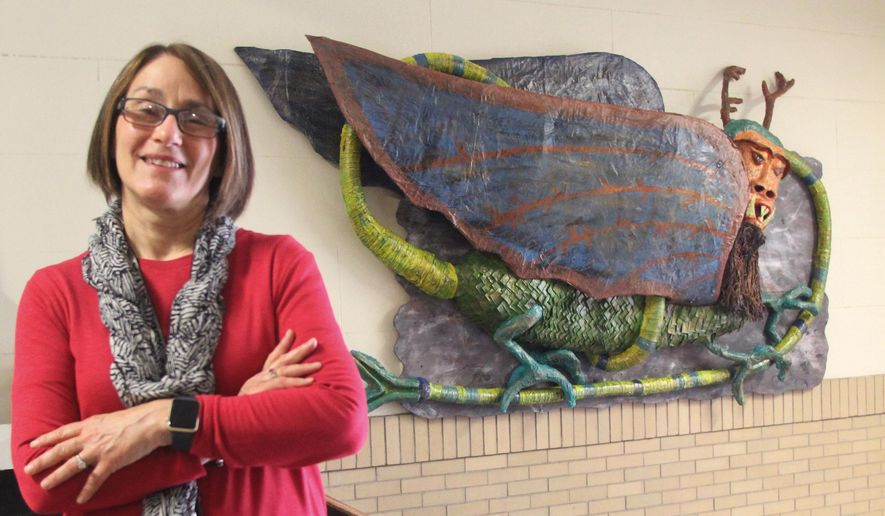 In this May 25, 2016, photo, Retiring Alton, Illinois Middle School art teacher Mimi Almonroeder stands in front of a paper mache version of the Piasa Bird that students made over the last school year in Alton, Ill. About 50 students in four separate classes worked on the project, which now hangs at the entrance to the Alton Middle School's Main Building. (Scott Cousins/The Telegraph via AP) BELLEVILLE NEWS-DEMOCRAT OUT; ST. LOUIS POST-DISPATCH OUT; MANDATORY CREDIT