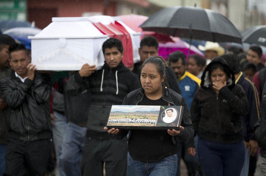 A young woman walks with a photo of Jesus Cadena, who died last Sunday during the clearing of the highway by police, as others carry his coffin in Nochixtlan, in Oaxaca state, Mexico, Tuesday, June 21, 2016. Violence erupted during the weekend in which at least 8 people died in confrontations between the police and striking teachers. The teachers are protesting against plans to overhaul the country's education system which include federally mandated teacher evaluations. (AP Photo/Eduardo Verdugo)