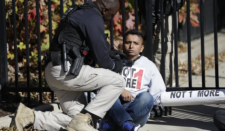 A police officer tries to free an immigration protester who chained himself to a gate in front of a building in Atlanta that houses federal immigration offices during a protest on Nov. 19, 2013. (Associated Press) **FILE**