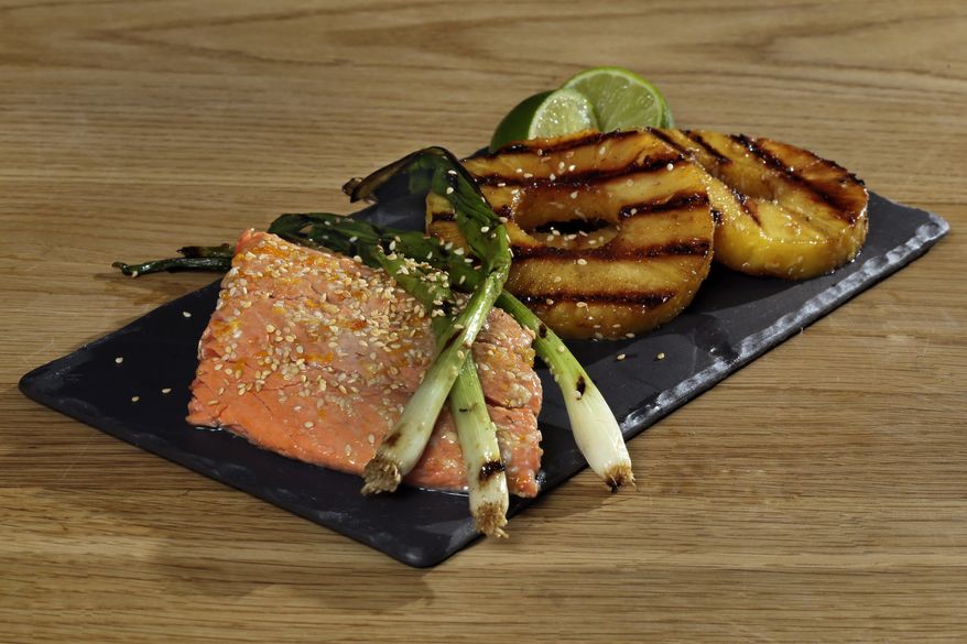 This May 23, 2016 photo shows grilled salmon, whole scallions and pineapple slices at the Institute of Culinary Education in New York. This dish is from a recipe by Elizabeth Karmel. (AP Photo/Richard Drew)