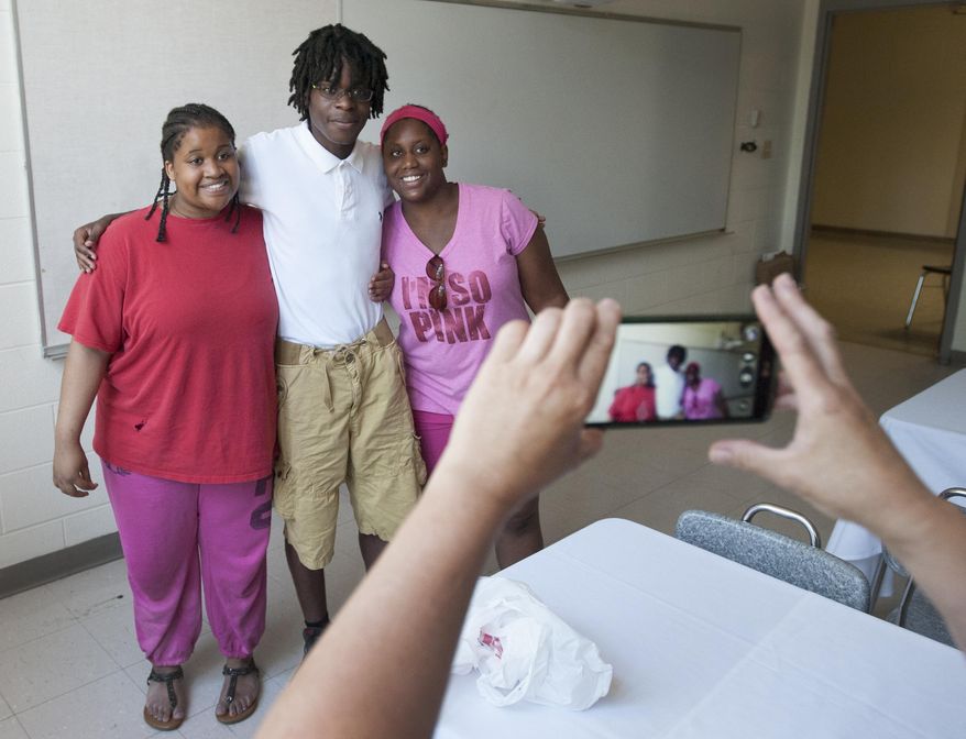 In this Wednesday, June 22, 2016, photo, Isaiah Cram poses for photos with his two half sisters, Vivica Gage, 18, left, and Michelle Gage, 21, during a reunion lunch at Jackson High School in Jackson, Mich. Cram, who is adopted, spotted Vivica at a school event and asked to meet her after realizing she was his sister. (J. Scott Park/MLive Media Group-Jackson Citizen Patriot via AP)