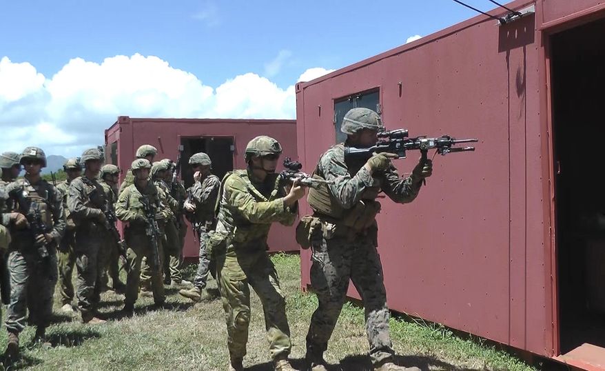 In this Thursday, July 7, 2016 photo, an Australian soldier, center left, and a U.S. Marine, right, get ready to raid a building at a mock urban combat training center in Kaneohe Bay, Hawaii. Australian soldiers are expected to lead a battalion of troops in the storming of a Hawaii beach during the world's largest maritime exercises this month, displaying the amphibious military skills they've been building up in recent years. (AP Photo/Audrey McAvoy)