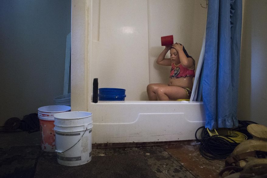 ADVANCE FOR USE SUNDAY, JULY 17 - In this photo taken June 30, 2016, Angelina Garcia, 9, bathes with rain water collected on buckets by her grandfather at their property in New King's Colony subdivision in Montgomery County, near New Caney, Texas. The family depends on bottled water and rain to shower and bathe because their home doesn't receive water service. (Marie D. De Jesus/Houston Chronicle via AP)