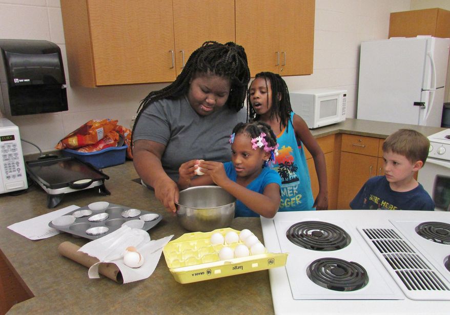 In this June 16, 2016 photo, counselor D'Aunniah Powell supervises and LaMara Cliff, 8, carefully cracks an egg at Camp Connections as Powell teaches kids how to make omelets in muffin tins in Decatur, Ill. Camp Connections' theme this summer is making healthy choices. (Valerie Wells/Herald & Review via AP)