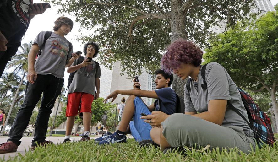 In this Tuesday, July 12, 2016, photo, Pokemon Go players Ana Valentina Ojeda, right, and Jaeden Valdespino, second from right, check their smartphones as they look for Pokemon at Bayfront Park in downtown Miami as the "Pokemon Go" craze has sent legions of players hiking around cities and battling with "pocket monsters" on their smartphones. (AP Photo/Alan Diaz) **FILE**