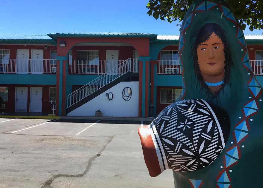 In this Wednesday, July 13, 2016 photo a charging station, center, at the Sandia Peak Inn along Albuquerque's Route 66 sits behind an American Indian statue, in N.M. Route 66, a highway made famous for attracting gas-guzzling Chevrolet Bel Airs traveling from Chicago to Los Angeles, is seeing a growing number of electric car charging stations along the 2,500-mile path, and some states are even pushing for solar panels and electric buses. (AP Photo/Russell Contreras)