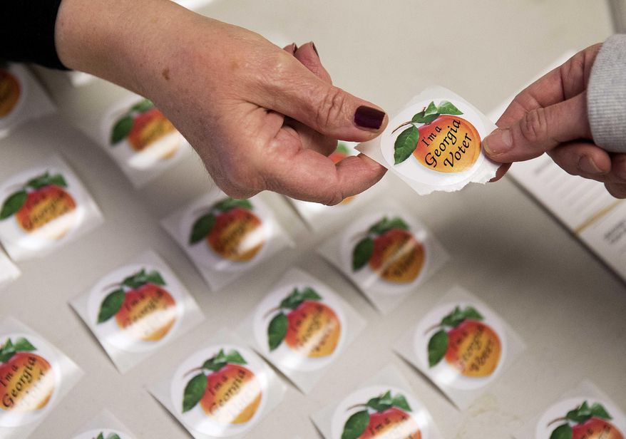 FILE - In this March 1, 2016 file photo, poll worker Delores Peterson, left, hands a sticker to a voter after they casted their ballot in Georgia's primary election at a polling site in Atlanta. Georgians have a week left to vote early in primary runoff elections set for July 26. Secretary of State Brian Kemp’s office reports that more than 53,000 people cast ballots for races around the state since July 5. (AP Photo/David Goldman)
