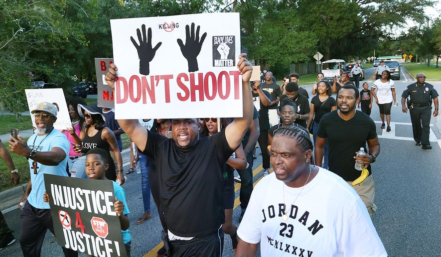 Mario Hicks, middle, holds a sign as he chants and marches during a Black Lives Matter march and rally in Sanford, Fla., Sunday, July 17, 2016. Sanford police chief Cecil Smith is pictured in the background at far right. (Stephen M. Dowell/Orlando Sentinel via AP)
