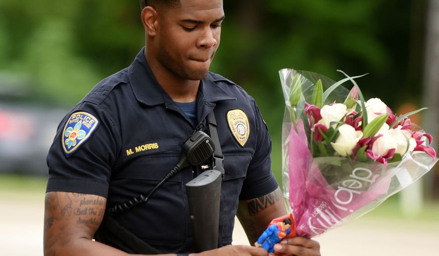 Baton Rouge Police Department Officer Markell Morris holds a bouquet of flowers and a Superman action figure that a citizen left at Our Lady of the Lake Hospital, where wounded police officers were brought after Sunday morning&#x27;s shootings. (The Times via Associated Press)