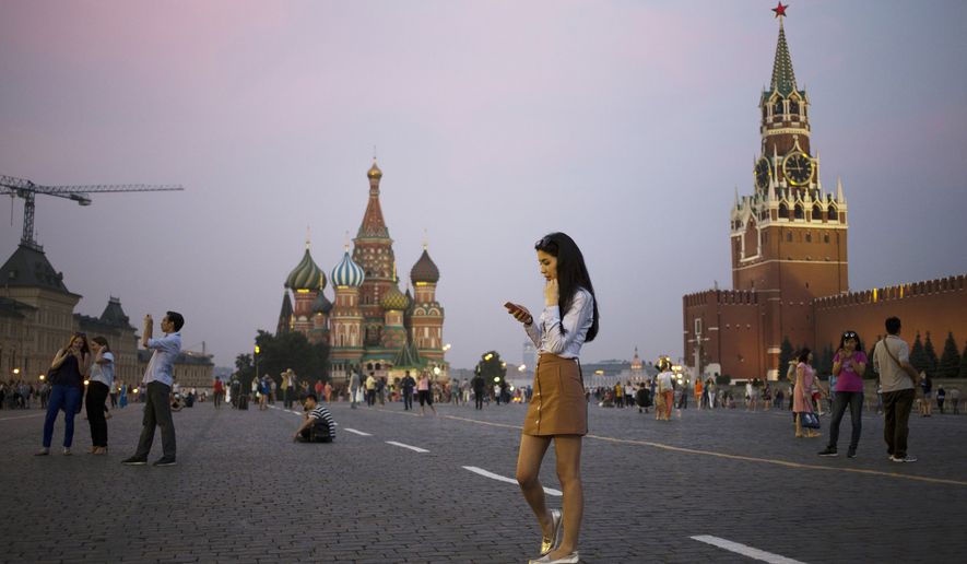 A young woman holds her smartphone at Red Square with the Kremlin&#39;s Spasskaya Tower, right, and St. Basil Cathedral, center, in the background in Moscow, Russia, Monday, July 25, 2016. (AP Photo/Pavel Golovkin)