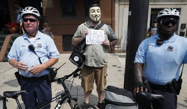 A Black Lives Matters protestor stands beside police officers during a protest march in downtown Philadelphia on Monday during the first day of the Democratic National Convention. (Associated Press)