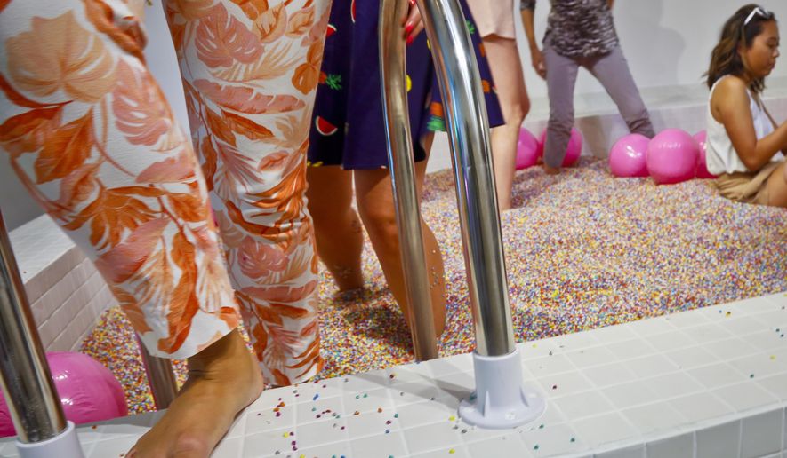 Visitors walk into a large pool filled with faux confetti-colored sprinkles, the biggest attraction of ice cream-themed works of art previewed at the Museum of Ice Cream, Thursday July 28, 2016, in New York. The museum opens on Friday and runs through Aug. 31. (AP Photo/Bebeto Matthews)