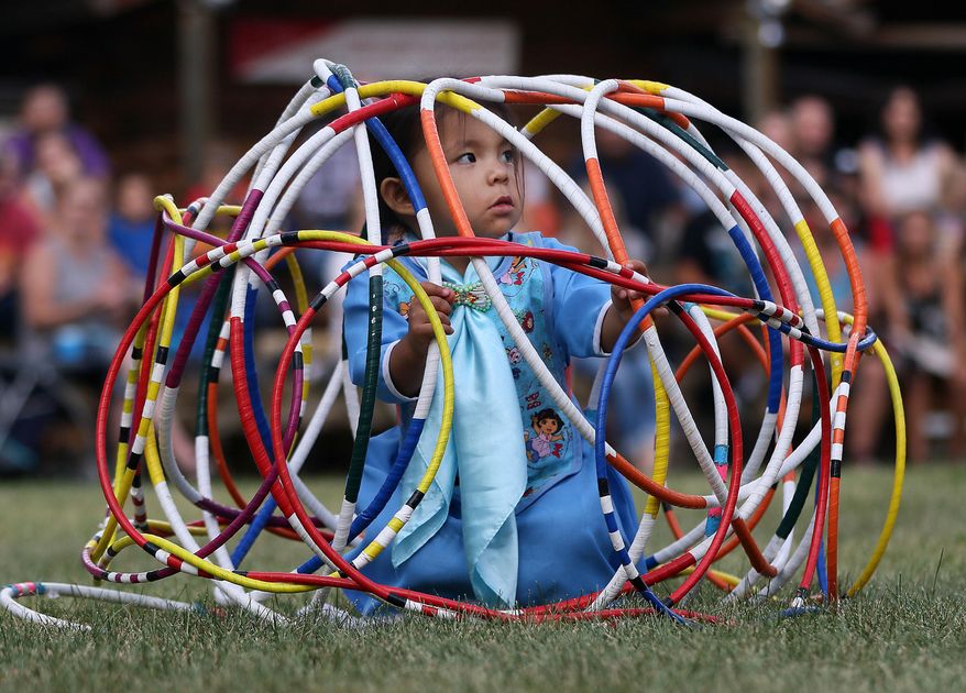 In this Saturday, July 23, 2016 photo, Aloysia Bell, 2, sits inside a "cage" of hoops as her mother finishes a hoop dance at the Indian Village at Frontier Park in Cheyenne, Wyo. The Indian Village adds to the Western story. The Wyoming Tribune Eagle reports that Sandi Iron Cloud's son said to her recently, "When you have cowboys, you have to have Indians, too." And Cheyenne Frontier Days organizers realized that after holding the very first event back in 1897. (Blaine McCartney/The Wyoming Tribune Eagle via AP)