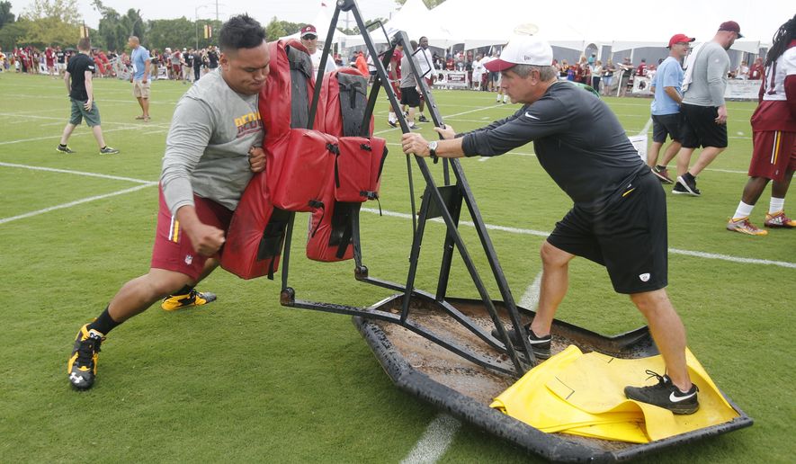 Washington Redskins guard Shawn Lauvao (77) works on the sled with offensive line coach, Bill Callahan, after the morning walk through at the Washington Redskins NFL football teams training camp in Richmond, Va., Saturday, July 30, 2016. (AP Photo/Steve Helber)