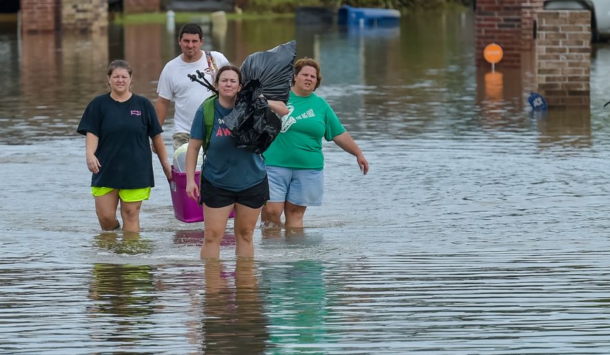 People wade in water near flood damaged homes in Highland Ridge Subdivision in Youngsville, La., Sunday, Aug. 14, 2016. Torrential rains swamped parts of southern Louisiana, causing widespread flooding. (Scott Clause/The Daily Advertiser via AP)