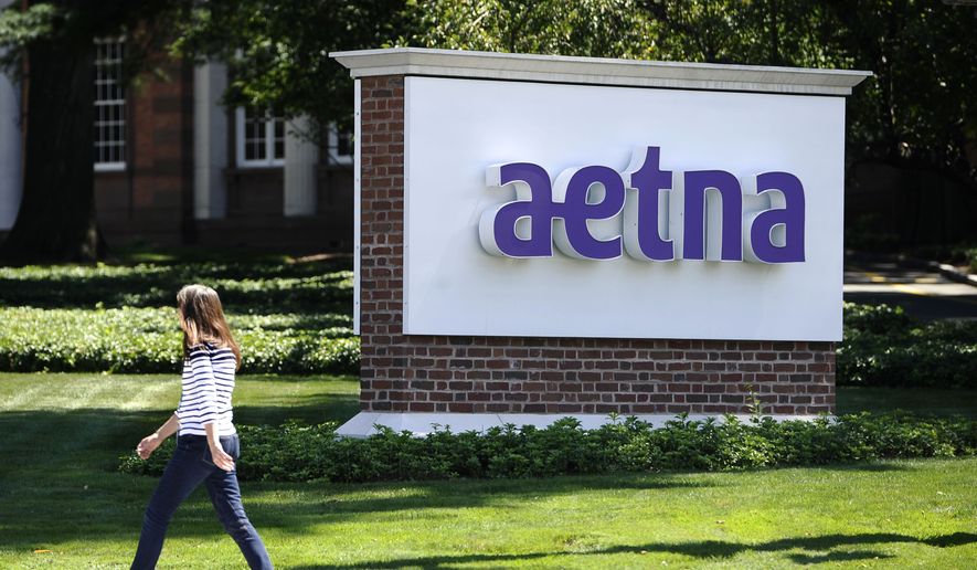 A woman walks past a sign for health insurer Aetna Inc., at the company headquarters in Hartford, Conn. (Associated Press)