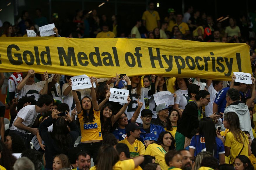 FILE - In this Aug. 12, 2016 file photo, fans hold signs against interim Brazilian President Michel Temer during a quarter-final match at the women's Olympic football tournament between Brazil and Australia in Belo Horizonte, Brazil. The smaller signs read in Portuguese: "Coup in Brazil" and "Get out Temer." Temer replaced President Dilma Rousseff as interim leader after she was suspended, and both have been at the epicenter of a corruption investigation that has led to the jailing of dozens of politicians and top businessmen. (AP Photo/Eugenio Savio, File)
