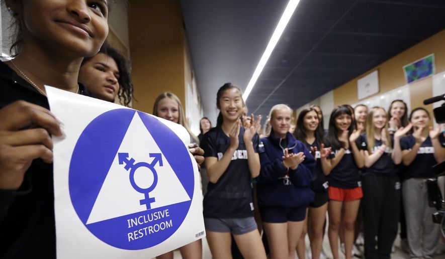 Deena Kennedy holds a sticker for a new gender neutral bathroom as members of the cheer squad applaud behind during a ceremonial opening for the restroom at Nathan Hale high school in Seattle on May 17, 2016. (Associated Press)