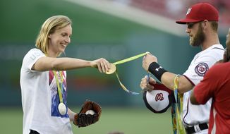 Olympic gold medal swimmer Katie Ledecky, left, hands her medals to Washington Nationals&#39; Bryce Harper, right, to hold before she threw out the ceremonial first pitch before a baseball game between the Baltimore Orioles and the Washington Nationals, Wednesday, Aug. 24, 2016, in Washington. (AP Photo/Nick Wass)