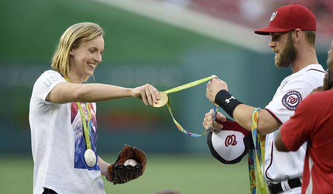 Olympic gold medal swimmer Katie Ledecky, left, hands her medals to Washington Nationals&#x27; Bryce Harper, right, to hold before she threw out the ceremonial first pitch before a baseball game between the Baltimore Orioles and the Washington Nationals, Wednesday, Aug. 24, 2016, in Washington. (AP Photo/Nick Wass)