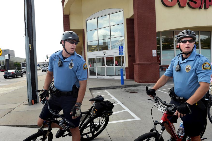 ADVANCE FOR USE MONDAY, AUG 29 - In this Wednesday, Aug. 17, 2016 photo, St. Paul bicycle patrol officers Jason Bain, left, and David Ratley ride through a drugstore parking lot in the Midway neighborhood of St. Paul, Minn. Four officers in the police department’s Western District have been assigned full-time to patrol on bicycles this summer. The pilot program was set up to address complaints about groups of young people hanging out on the streets, sometimes getting into fights, shoplifting or other trouble, along the Central Corridor rail line, according to police spokesman Steve Linders. Scott Takushi/Pioneer Press via AP)