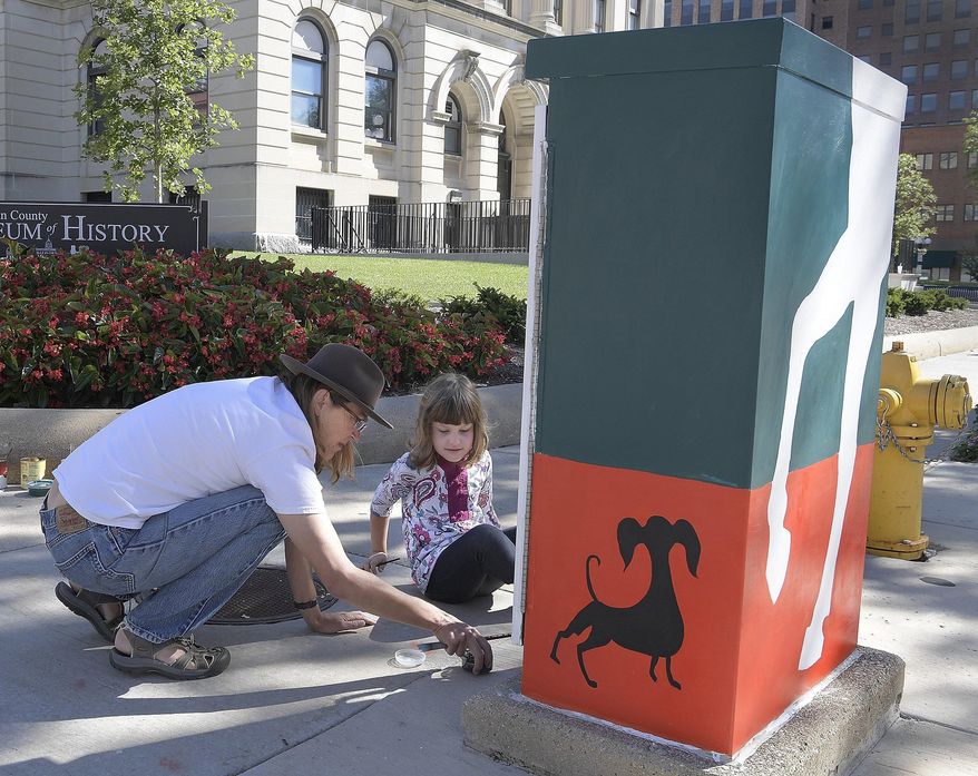 In this Aug. 21, 2016 photo, artist Danell Dvorak gets a little help from her friend, Emma Shannabarger, while painting the traffic control box in downtown Bloomington, Ill. Dvorak's love of horses combined with a curious dog and a circus theme complete her design for the box. A metal traffic signal control box doesn't appear to be an ideal canvas for a work of art, but that's where several local artists are adding splashes of color in Bloomington. (Lori Ann Cook-Neisler/The Pantagraph via AP)