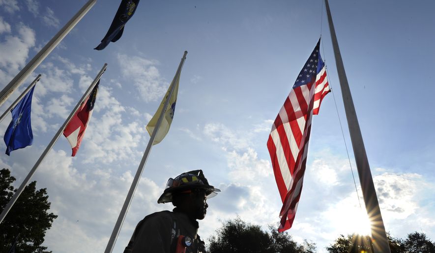 As the early morning sun begins to break above the trees, firefighter Alwyn Chandler, with the Fort Gordon Fire Department, stands beneath the flag following a 9/11 remembrance ceremony at Fort Gordon, Ga., Friday,  Sept. 9, 2016.   (Michael Holahan/The Augusta Chronicle via AP)