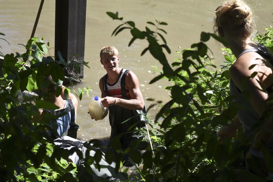 In this May 29, 2015 photo, Cody Nelson hands Payton Nelson a jug full of water from the Shell Creek near Newman Grove for use in tests to determine the creeks water quality in Newman Grove, Neb. Since 1988, complaints of fish kills in the creek have attracted the attention of groups from the Lower Platte North Natural Resources District to law enforcement. The water pooled cloudy and pungent in some places, and streamed by with contaminants where it flowed. (Marcella Mercer /The Norfolk Daily News via AP)