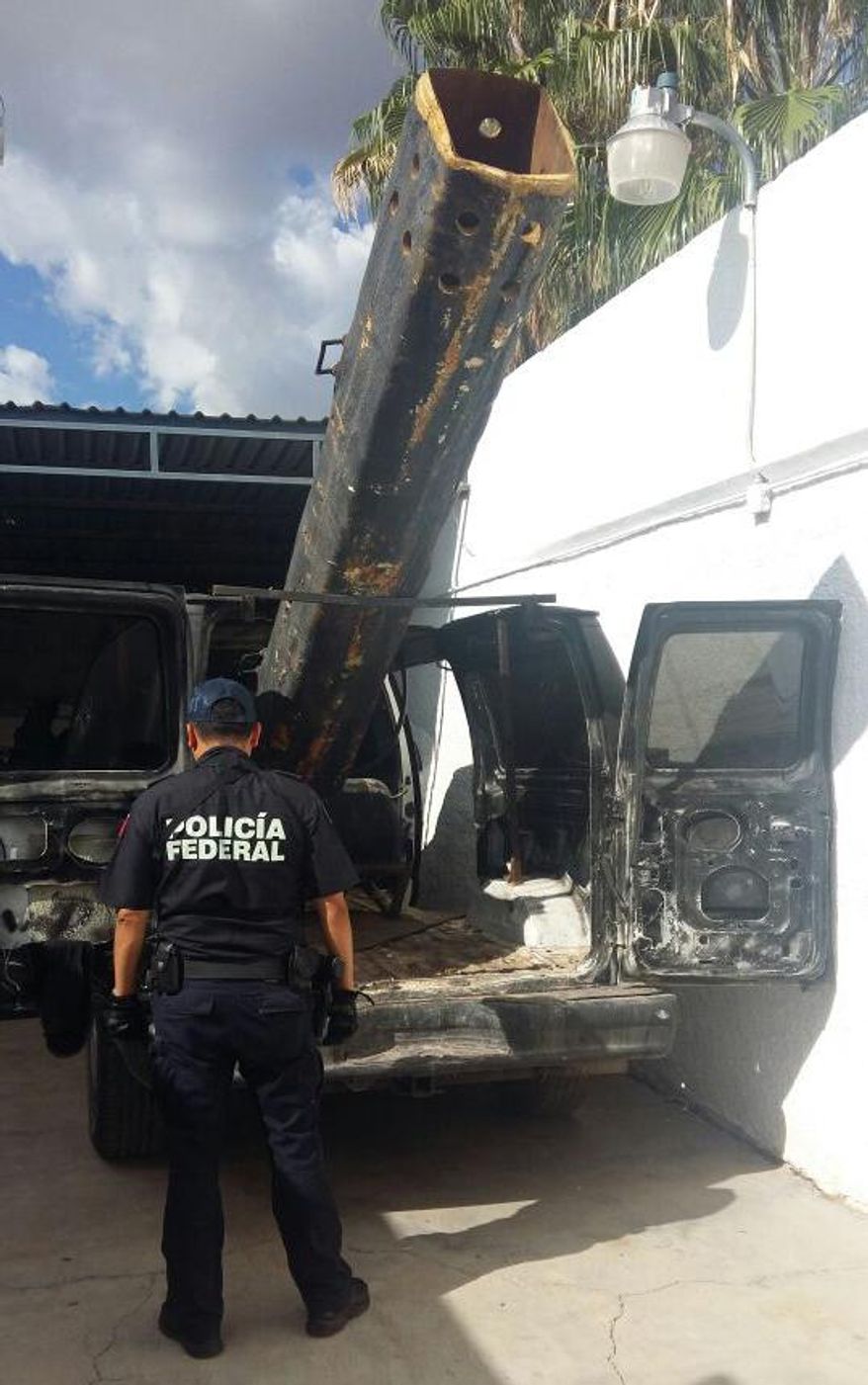 In this Sept. 17, 2016 photo released by Mexico Federal Police, an officer stands next to a van outfitted with a 10-foot (3-meter) air cannon in Agua Prieta, Mexico, along the border with Douglas, Arizona. According to federal police, it was used to shoot projectiles into the U.S. and the van was reported stolen from the city of Hermosillo in the Mexican state of Sonora over the summer. a U.S. Border Patrol spokesman said that the most common common use for this sort of device is lobbying marijuana packages over the border fence. (AP Photo/Policia Federal Preventiva)