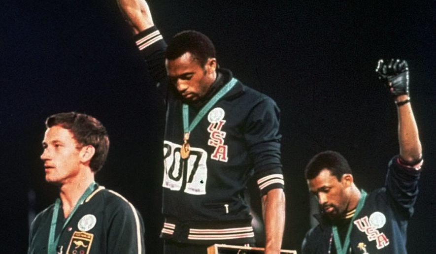 U.S. athletes Tommie Smith, center, and John Carlos stare downward while extending gloved hands skyward during the playing of the Star Spangled Banner after Smith received the gold and Carlos the bronze for the 200 meter run at the Summer Olympic Games in Mexico City, Oct. 16, 1968. Australian silver medalist Peter Norman is at left. They called it a &quot;human rights salute.&#x27;&#x27; (AP Photo/File) **FILE**