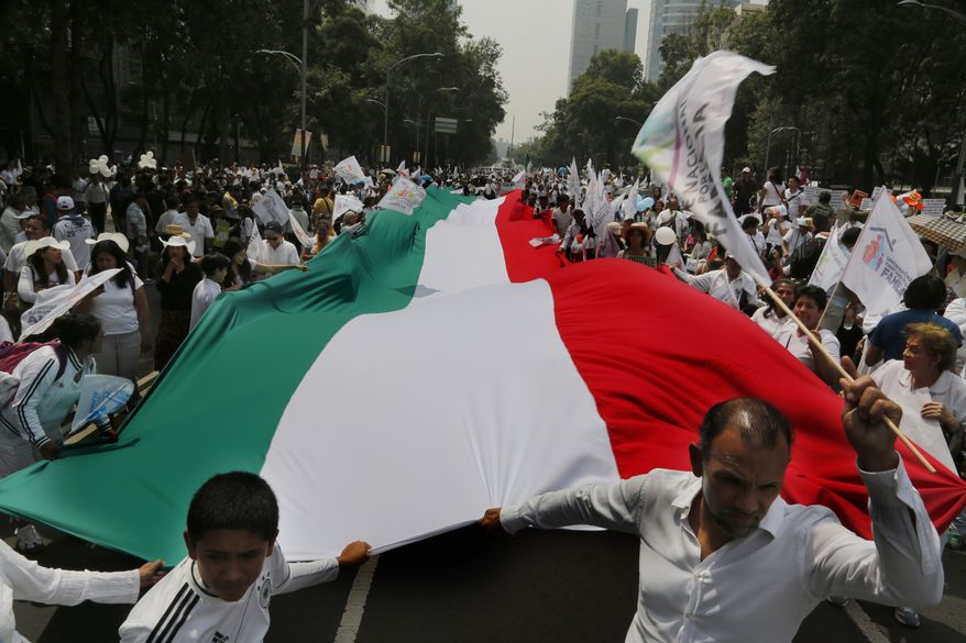 Demonstrators walk with a giant Mexican national flag during a march organized by representatives of the National Front for the Family, in Mexico City, Saturday, Sept. 24, 2016. Dueling marches, in support and against Mexican President Enrique Pena Nietos push to legalize same-sex marriage, gathered at the Angel of Independence monument. The two sides were kept apart Saturday by hundreds of police and barriers erected around the city's iconic monument. (AP Photo/Marco Ugarte