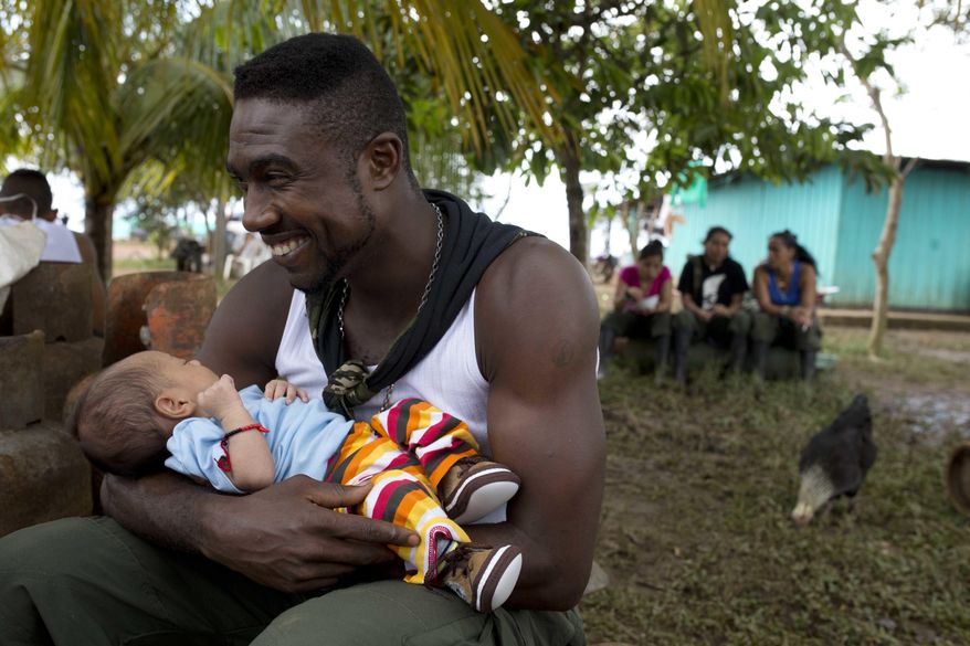 Diomedes holds the baby of a visiting relative of a fellow rebel of the Revolutionary Armed Forces of Colombia, FARC, in the Yari Plains, southern Colombia, Sunday, Sept. 25, 2016. President Juan Manuel Santos and FARC leader Rodrigo Londono, alias Timochenko, are expected to sign a peace accord to end more than five decades of conflict Sept. 26 in the Caribbean city of Cartagena. (AP Photo/Ricardo Mazalan)