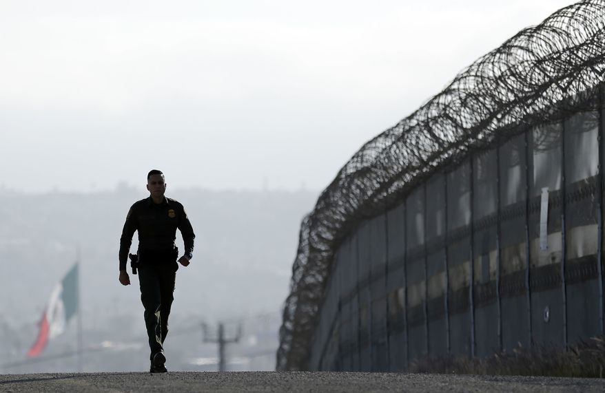 Border Patrol agent Eduardo Olmos walks near the secondary fence separating Tijuana, Mexico, and San Diego. (Associated Press) ** FILE **
