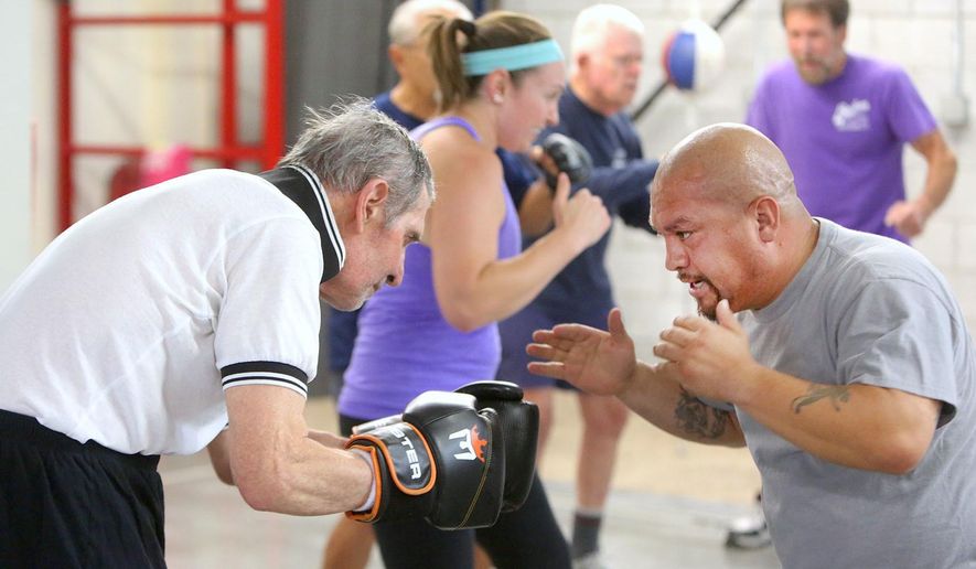 In this Monday, Sept. 19, 2016 photo, trainer Cisco Rodriguez, right, helps first-time Parkinson's boxing participant Tom Pecsvaradi with a warm-up exercise at the Tazmanian Boxing Club in Carson City, Nev. (Jim Grant/Nevada Appeal via AP)