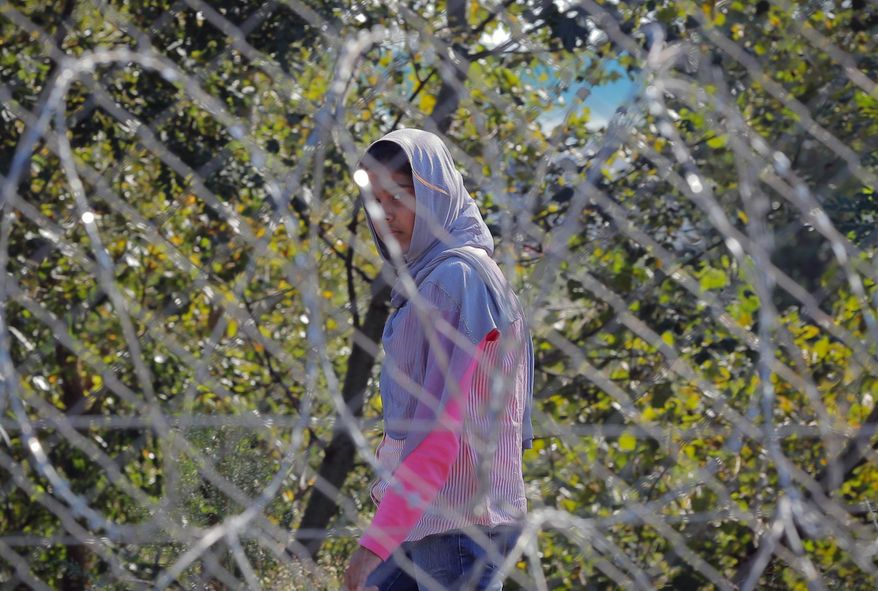 A migrant girl walks behind a barbed wire fence at a makeshift camp in Horgos, Serbia, seen from the Hungarian side of the border, Friday, Sept. 30, 2016. Hungarians will vote Sunday in a referendum which Prime Minister Viktor Orban hopes will give his government the popular support it seeks to oppose any future plans by the European Union to resettle asylum seekers among its member states.(AP Photo/Vadim Ghirda)