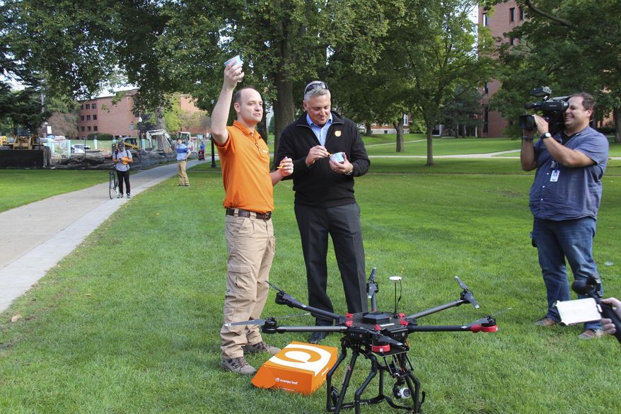 In a photo form Oct. 4, 2016, Orange Leaf Frozen Yogurt franchise owner Jeremy Latchaw, left, and president Geoff Goodman sample the frozen yogurt delivered by a drone to the Hope College campus in Holland, Mich. Dubbed "Project Flying Orange Unicorn," the business says it's planning to offer deliveries from its Orange Leaf Holland store located a few blocks from campus. The effort is led by Latchaw who is also president of Mishigami Group, a drone business that's working with fire and police departments to develop unmanned aerial vehicle programs. (Erin Dietzer/The Holland Sentinel via AP)