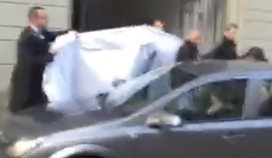 FILE- In this Wednesday, May 27, 2015 file picture taken from a cell phone video, hotel employees hold a blanket to hide the identity of a person led out of a side entrance of the Baur au Lac hotel to a waiting car in Zurich, Switzerland. FIFA is no longer hosting its executives at the waterside super-luxurious, lake-side hotel where Swiss police launched dawn raids last year. (AP Photo/Rob Harris, File)
