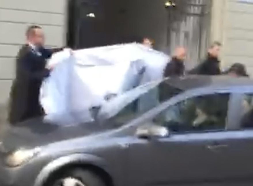 FILE- In this Wednesday, May 27, 2015 file picture taken from a cell phone video, hotel employees hold a blanket to hide the identity of a person led out of a side entrance of the Baur au Lac hotel to a waiting car in Zurich, Switzerland. FIFA is no longer hosting its executives at the waterside super-luxurious, lake-side hotel where Swiss police launched dawn raids last year. (AP Photo/Rob Harris, File)