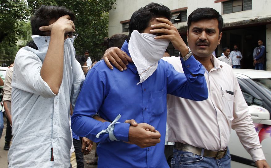 A police official, right, escorts two men outside the court in Thane, outskirts of Mumbai, India, Thursday, Oct. 6, 2016. Indian police have arrested 70 people and are questioning hundreds more after uncovering a massive scam to cheat thousands of Americans out of millions of dollars by posing as U.S. tax authorities and demanding unpaid taxes. (AP Photo/Rajanish Kakade)