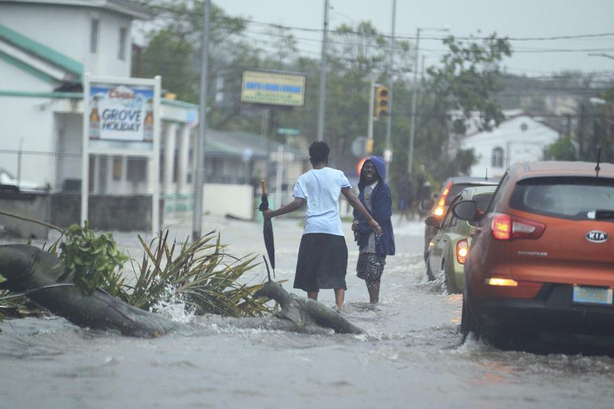 Residents and vehicles avoid a downed tree and power cable along a flooded roadway in the aftermath of Hurricane Matthew in Nassau, Bahamas, Thursday, Oct. 6, 2016. The head of the Bahamas National Emergency Management Authority, Capt. Stephen Russell, said there were many downed trees and power lines, but no reports of casualties. (AP Photo/Tim Aylen)