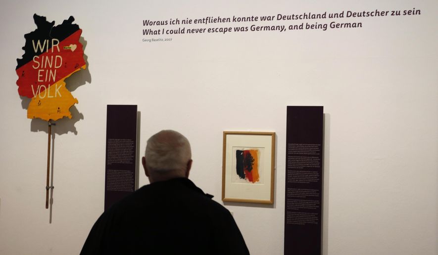 A man looks at the work 'Eagle' by Georg Baselitz, right, and a poster 'We are one people' by Eckart Conradt that was carried during a protest in Berlin's Lustgarten in December 1989 during a press preview for the exhibition 'The British view' in the Gropius-Bau in Berlin, Germany, Friday, Oct. 7, 2016. The exhibition 'The British View: Germany – Memories of a Nation' runs through Jan. 9, 2017. (AP Photo/Ferdinand Ostrop)