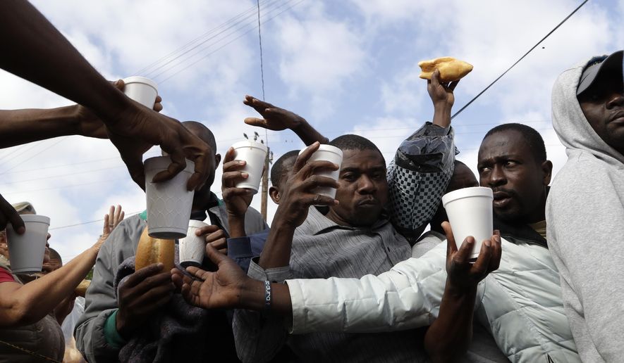 In this Oct. 3, 2016 photo, Haitian migrants receive food and drinks from volunteers as they wait in line at a Mexican immigration agency in Tijuana with the hope of gaining an appointment to cross to the U.S. side of the border. Many Haitians arriving at the Mexico-U.S. border are unaware of a new U.S. policy of putting them in deportation proceedings and detaining them while making efforts to fly them home. (AP Photo/Gregory Bull)