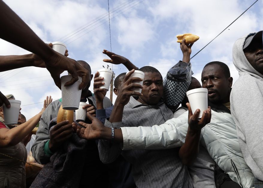 In this Oct. 3, 2016 photo, Haitian migrants receive food and drinks from volunteers as they wait in line at a Mexican immigration agency in Tijuana with the hope of gaining an appointment to cross to the U.S. side of the border. Many Haitians arriving at the Mexico-U.S. border are unaware of a new U.S. policy of putting them in deportation proceedings and detaining them while making efforts to fly them home. (AP Photo/Gregory Bull)