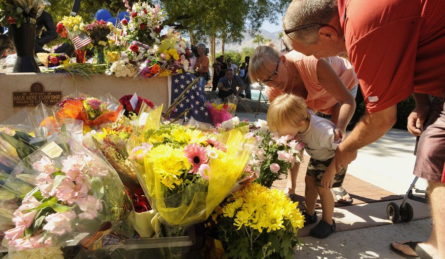 Two-year-old Jayden Bunnell kisses flowers at the urging of his grandparents Barbara Bunnell and J.D. Bunnell, from Cathedral City, Calif., for slain Palm Springs Police Officers Jose "Gil" Gilbert Vega and Lesley Zerebny, in front of the police station in Palm Springs, Calif., Sunday, Oct. 9, 2016. Vega and Zerebny, trying to resolve a family dispute, were killed Saturday when a man they had been speaking with suddenly pulled out a gun and opened fire on them, the city's police chief said. (AP Photo/Rodrigo Pena)