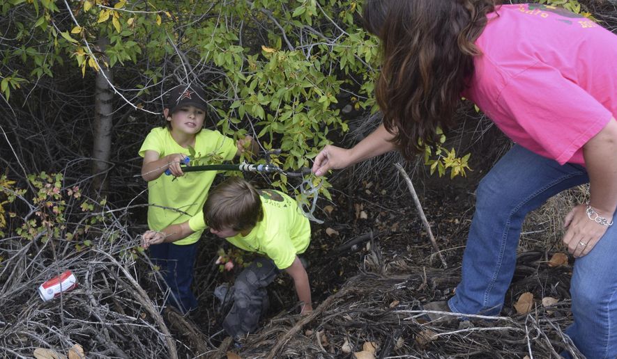 In this Sept. 23, 2016 photo, Quincy Barhaug passes up a piece of trash up to his mother, Jamie Barhaug, while Devon Barhaug reaches for a beer can in precipitous and precarious footing, south of Powell, Wyo. (Gib Mathers /The Powell Tribune via AP)