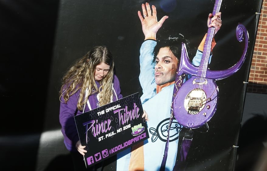A Prince fan poses with a large photo backdrop of the late Prince as fans gather outside Xcel Arena Thursday, Oct. 13, 2016, in St. Paul, Minn., waiting for a concert honoring the musician who died in April of accidental painkiller overdose. (AP Photo/Jim Mone)